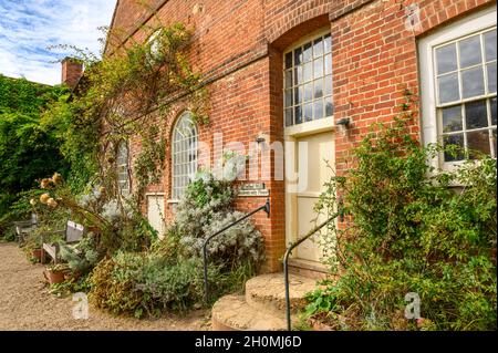 Rote Backsteinfassade der historischen Flatford Mill mit Kletterpflanzen und Bänken in Flatford, Suffolk, England. Stockfoto