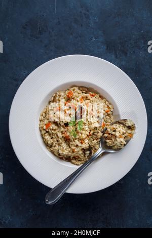 Risotto, italienischer Reis mit Pilzen, Gemüse und Petersilie auf weißem Porzellanteller serviert Stockfoto