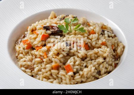 Risotto, italienischer Reis mit Pilzen, Gemüse und Petersilie auf weißem Porzellanteller serviert Stockfoto