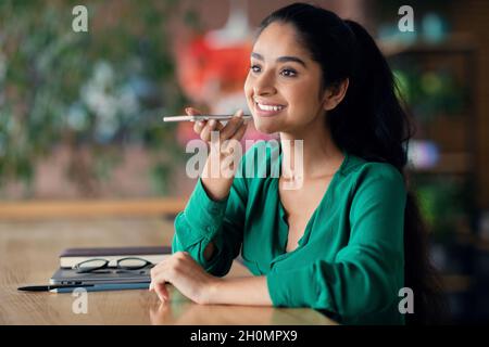 Glückliche indische Frau, die Sprachnachricht auf dem Handy aufzeichnete Stockfoto