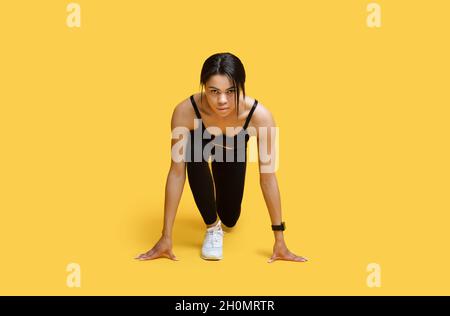 Sprint-Konzept. Junge afroamerikanische Athletin in Startposition bereit zum Laufen, gelber Hintergrund Stockfoto