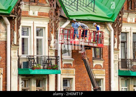Arbeiter auf einer Hebebühne, die das Dach eines historischen modernistischen Gebäudes repariert. Wartungs- und Umbauarbeiten in St. Petersburg Russland Stockfoto