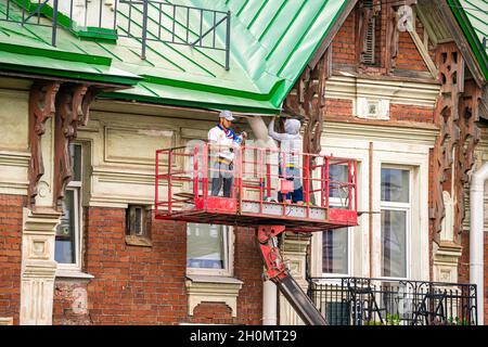 Arbeiter auf einer Hebebühne, die das Dach eines historischen modernistischen Gebäudes repariert. Wartungs- und Umbauarbeiten in St. Petersburg Russland Stockfoto