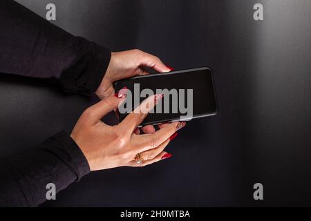 Weibliche Hände mit schönen Fingernägeln halten schwarzes Telefon auf schwarzem Hintergrund und. Stockfoto