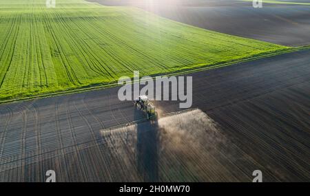 Luftbild des Traktors, der im Frühjahr im Feld Boden und Jungpflanzen spritzt Stockfoto