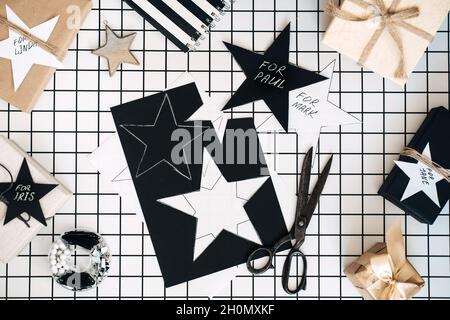 Personalisierte Geschenke. Modernes Schwarz-Weiß-Flachlappen mit Geschenkverpackung für Weihnachten. Scheren, eingewickelte Bastelkisten mit Namen und Verpackung Stockfoto