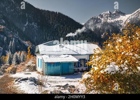 Berglandschaft des Herbstwaldes mit gelben Bäumen und Schnee und Haus im Dorf weißen Gipfel in Kasachstan Stockfoto