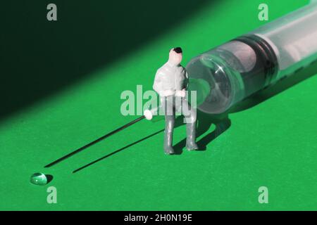 Miniaturmann sitzt auf einer Spritzennadel auf grünem Hintergrund. Stockfoto