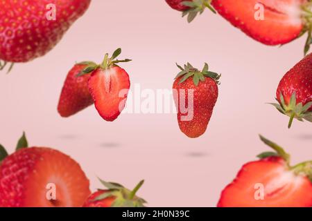 Kreative Idee mit schwebenden reifen Erdbeeren auf einem pastellrosa Hintergrund. Vitamine, frische gesunde Ernährung Konzept. Minimaler Fruchtansatz. In Scheiben Geschnitten Stockfoto