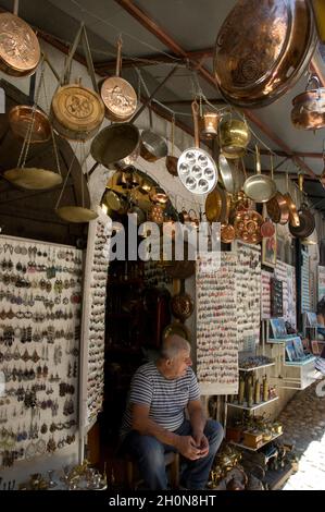 Ein Mann sitzt vor einem Souvenirladen - Mostar in Bosnien und Herzegowina ist berühmt für seine Stari Most, alte osmanische Brücke, die überquert Stockfoto