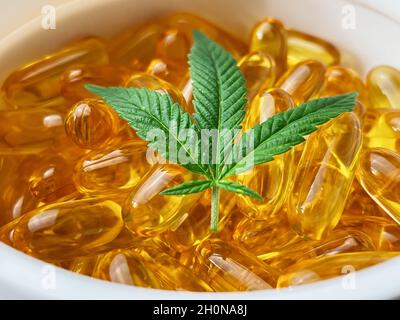 Nahaufnahme eines Behälters, der mit CBD-Weichgelkapseln und Cannabisblatt, alternativer Medizin, gefüllt ist Stockfoto