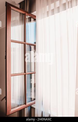 Vertikales Ajar-Fenster und helles Licht durch transparente Vorhänge Stockfoto