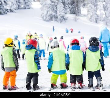 Gruppe kleiner Kinder mit Helmen und Westen, die auf Skiern stehen und Grundkenntnisse für das Skifahren bei Polygon erlernen Stockfoto