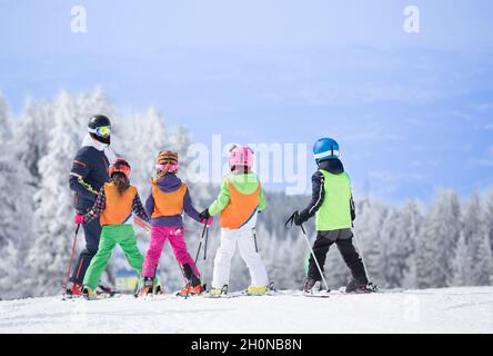 Eine Gruppe von Kindern, die mit einem Skilehrer Skifahren lernen. Blauer Himmel und weiße Tannen im Hintergrund Stockfoto