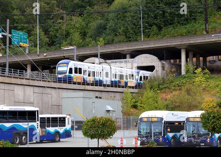 Ein Sound Transit Link-Zug fährt in den Beacon Hill Tunnel in Seattle Sodo ein, wobei die Autobahn Interstate 5 oben und ein Parkplatz für Pendlerbusse darunter liegen. Stockfoto