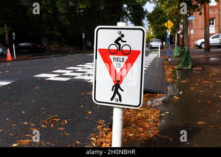 Ein Fahrradfahrer erbringt ein Fußgängerschutzschild auf einem Radweg, der eine Bushaltestelle an der NW 18th St in Portland, Oregon, kreuzweise. Bus-Glühbirne Stockfoto