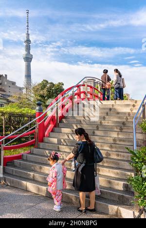 tokio, japan - oktober 26 2019: Kleines Mädchen im Kimono mit ihrer Mutter am Fuß der Treppe der traditionellen roten Taikobashi-Brücke, die von Skytree überblickt wird Stockfoto