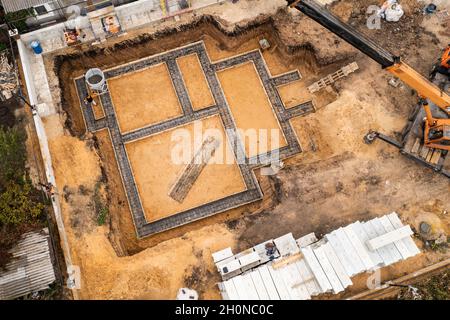 Gründung eines zukünftigen Hauses. Gießfundament mit Zement auf Baustelle mit Kran, Luftaufnahme. Stockfoto