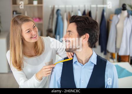 Schneider steht in der Nähe des männlichen Klienten und misst den Rücken Stockfoto