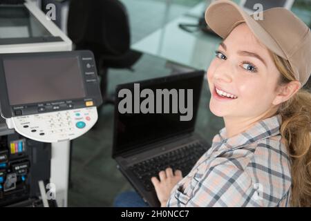 Glückliche Frau lächelt der Kamera zu, die einen Drucker repariert Stockfoto