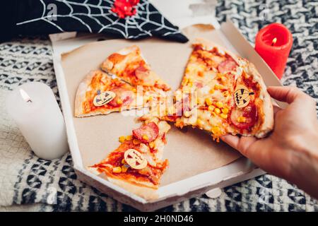 Helloween Pizza mit kleinen Papierkarren-O-Laternen-Kürbissen. Feiertagsfeier mit Kerzen und Kostümen. Halten Stück Pizza mit Halloween-Symbol auf fo Stockfoto