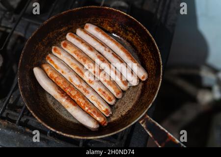 Gebackene dünne lange Schweinefleischwürste in Naturdarm auf der alten gegossenen Bratpfanne auf rustikalem Tisch, Draufsicht Stockfoto