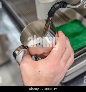 Nahaufnahme der Hände eines Barista, der warme Milch auf einer Kaffeemaschine aufschäumt, um Cappuccino oder Latte in einem Café zuzubereiten. Quadratisches Foto Stockfoto