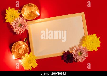 Frohes Diwali. Diya Öllampe und Blumen auf rotem Hintergrund. Feier des traditionellen indischen Festivals des Lichts. Leerer Rahmen für Text. Stockfoto