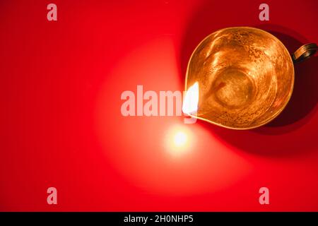 Brennende Diya-Öllampe auf rotem Hintergrund. Feier des traditionellen indischen Festivals des Lichts. Frohes Diwali. Speicherplatz kopieren. Stockfoto