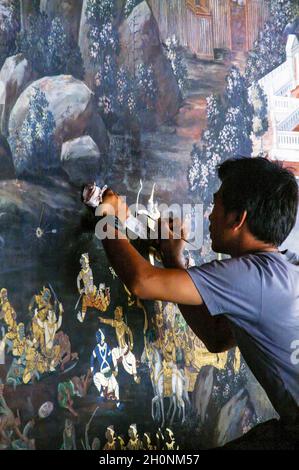 Ein junger Künstler repariert Schäden und Verblassen an den Wandgemälden. Ramakien. Wat Phra Kaeo, Grand Palace, Bangkok, Thailand. Blattgold, vergoldet. Stockfoto