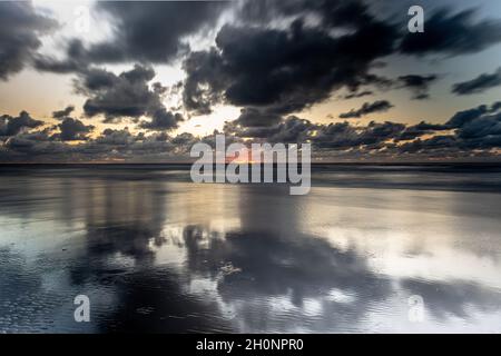 Orangefarbener Sonnenuntergang durch düstere Wolken über dem ruhigen Meer Stockfoto