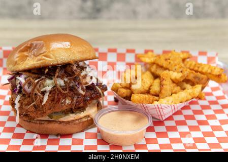 Würziges, heißes Hühnchen-Sandwich mit Zwiebeln und Gurken, gekrönt mit cole Slaw und serviert mit einer Dipping-Sauce. Stockfoto