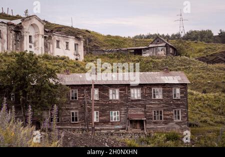 Altes, verlassenes zweistöckiges Holzgebäude in einer verlassenen Altstadt oder einem Dorf am Hang des Hügels, umgeben von ähnlich halb ruinierten Häusern Stockfoto