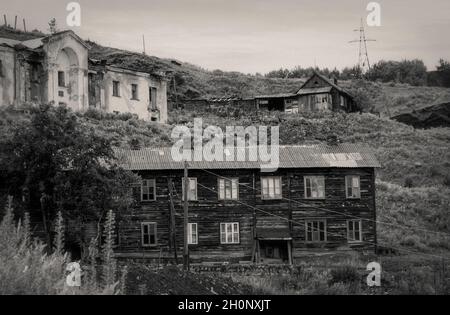 Altes, verlassenes zweistöckiges Holzgebäude in einer verlassenen Altstadt oder einem Dorf am Hang des Hügels, umgeben von ähnlich halb ruinierten Häusern Stockfoto