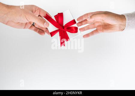 Schöne Feiertage oder Weihnachten Hintergrundbild eines kaukasischen männlichen Hand geben eine kleine rote Band verpackt Geschenkbox an eine gemischte Rasse Afroamerikaner Stockfoto