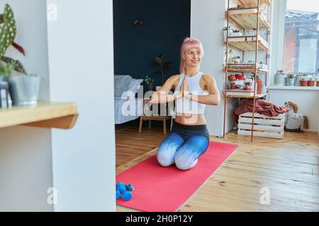 Weibliches Modell im Trainingsanzug hält die Hände in namaste Mudra, die auf den Knien auf der Matte sitzt Stockfoto
