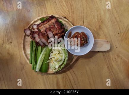 Kohlebrochenem Schweinehals (gegrilltes Schweinefleisch) und Gemüse (Gurke, Kohl) serviert mit würziger Dip-Sauce (Jaew) auf einem Holztablett Ready to Eat. Stockfoto