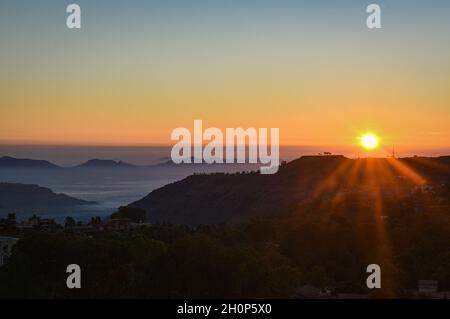 Sonnenaufgang am frühen Morgen vom Hügel, Sonnenstrahlen und Nebel über den Bergen Stockfoto