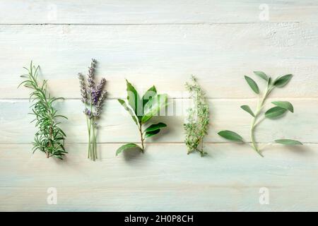 Frische aromatische Kräuter, oben flach auf einem hölzernen Hintergrund. Rosmarin, Lavendel, Lorbeerblatt, Thymian und Salbei, kulinarische Pflanzen Stockfoto