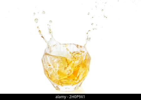 Glas Whiskey mit Eis und Spritzern auf weißem Hintergrund mit Reflexion. Stockfoto