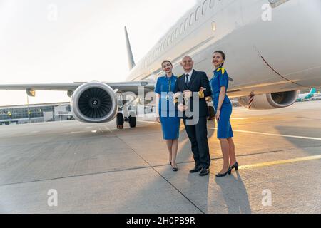 Glücklicher Pilot und Flugbegleiter stehen in der Nähe des großen Flugzeugs zusammen Stockfoto