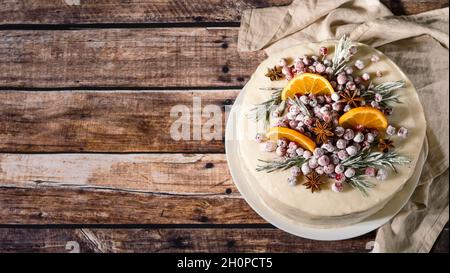 Winter hausgemachter Kuchen auf Holzhintergrund. Weisse Sahnetorte mit Rosmarin, Preiselbeeren, Sternanise und Orangen in Scheiben. Speicherplatz kopieren. Draufsicht Stockfoto
