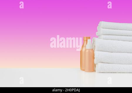 Stapel Handtücher, Flaschen mit Shampoo auf weißem Tisch Stockfoto