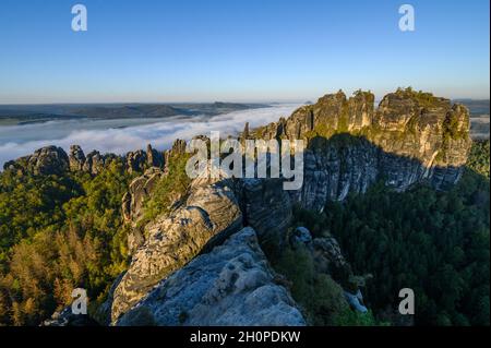 Bad Schandau, Deutschland. Oktober 2021. Blick vom Aussichtspunkt Schrammstein in der Sächsischen Schweiz auf die Felsen der Schrammsteine und den vorbeiziehenden Nebel im Elbtal. Das Niedergebirge, das überwiegend aus Sandstein besteht, erstreckt sich über rund 700 Quadratkilometer am oberen Elbbereich. Der deutsche Teil heißt Sächsische Schweiz, der tschechische Teil Böhmische Schweiz. Quelle: Robert Michael/dpa-Zentralbild/dpa/Alamy Live News Stockfoto