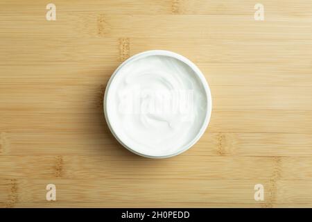 Kosmetische Creme Hintergrund. Weiße Kosmetikcreme für Haut und Körper in einem offenen weißen Glas auf einem leeren Hintergrund aus Holzbambus. Hochwertige Fotos Stockfoto