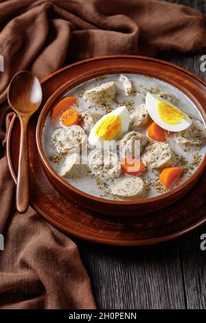 Zuek polieren fermentierte Roggensuppe mit traditioneller polnischer weißer Kielbasa oder Wurst mit Majoran, hart gekochte Eier, die auf einer Tonschüssel mit einer Holzschale serviert werden Stockfoto