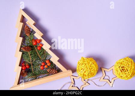 Hölzerner weihnachtsbaum mit Tannenzweigen innen verziert mit Vogelbeeren auf purpurem Papierhintergrund mit Rattankugeln Stockfoto