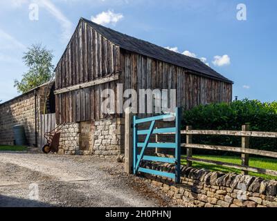 Alte hölzerne Scheune auf einem Steinfundament über ein blaues Tor, Baslow, Derbyshire, Großbritannien, angefahren Stockfoto