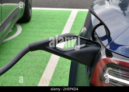 Nahaufnahme eines Elektroautos, der zum Aufladen in den energiesparenden Steckdosen an der Tankstelle eingesetzt wird. Draußen an einem trockenen Herbsttag Stockfoto