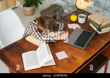 High-Angle-Ansicht des müden kleinen Schulmädchen, das auf dem Schreibtisch schläft und auf Notebooks liegt, und des erschöpften Schulmädchen, das sich faul und unmotiviert fühlt Stockfoto